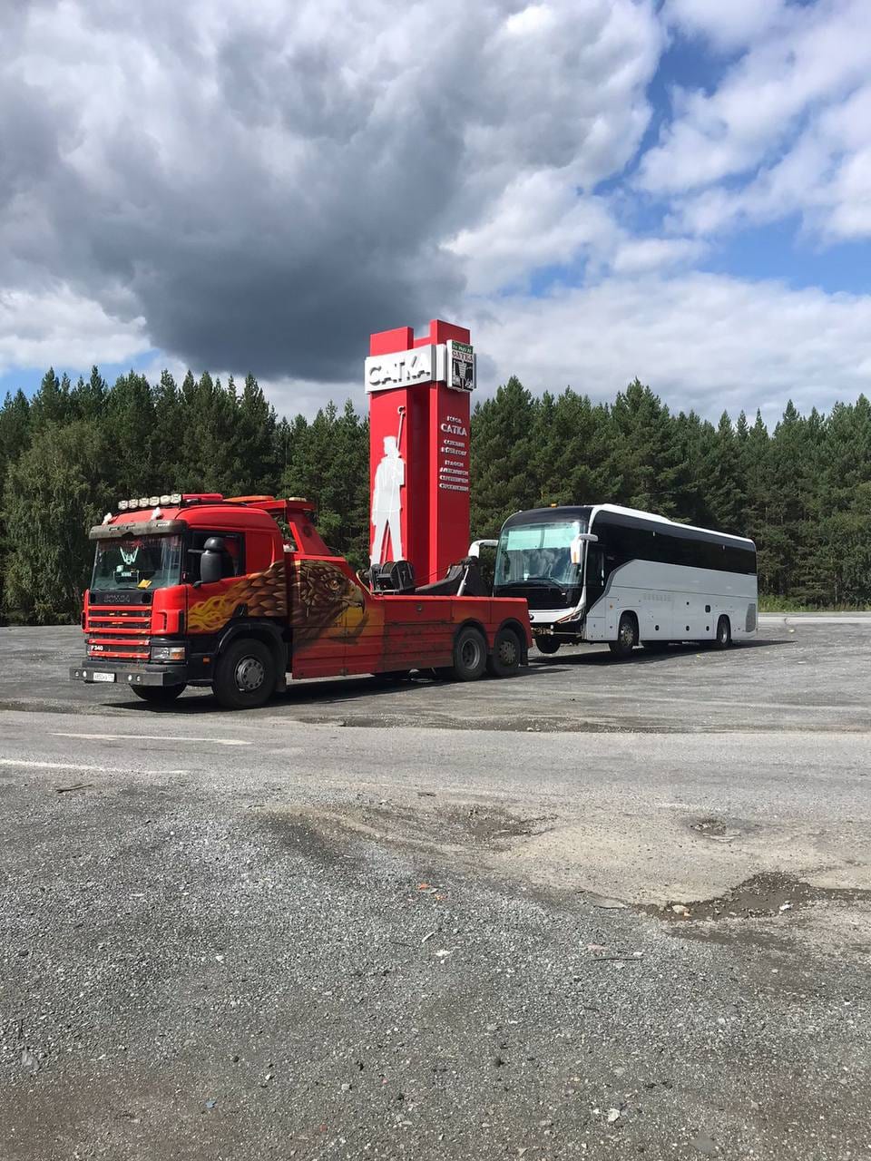 Эвакуатор Scania буксирует туристический автобус у въездной стелы «Сатка»